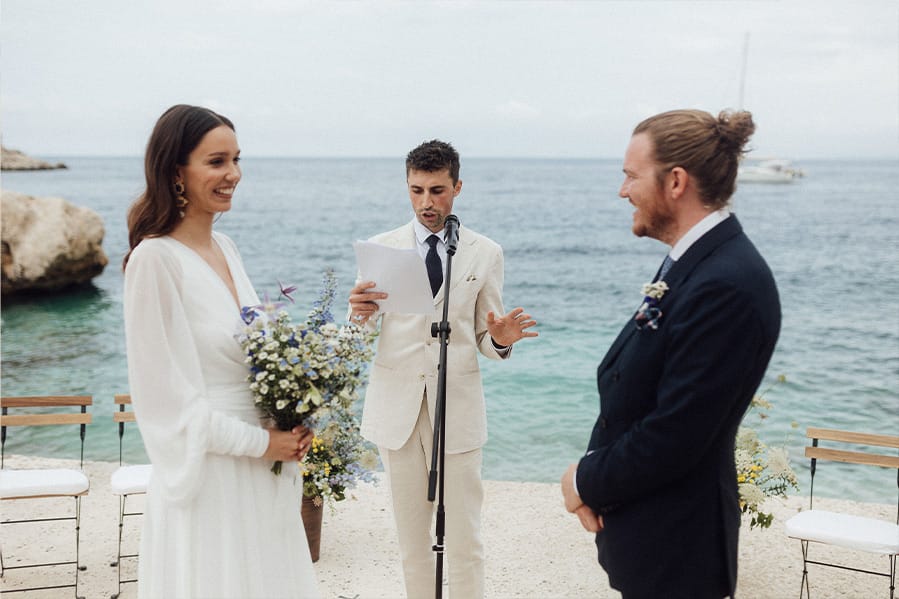 A wedding on a waterfront with a happy couple and their friend officiant.