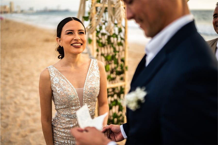 A bride standing on the beach looking fondly at her soon-to-be spouse.